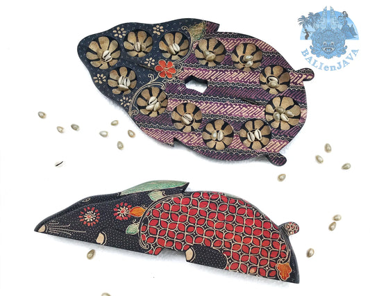 Two wooden rabbit-shaped board games with intricate patterns, one in black and beige with beige accents, and the other in black and red with green accents, displayed on a white background with scattered cowrie shells.