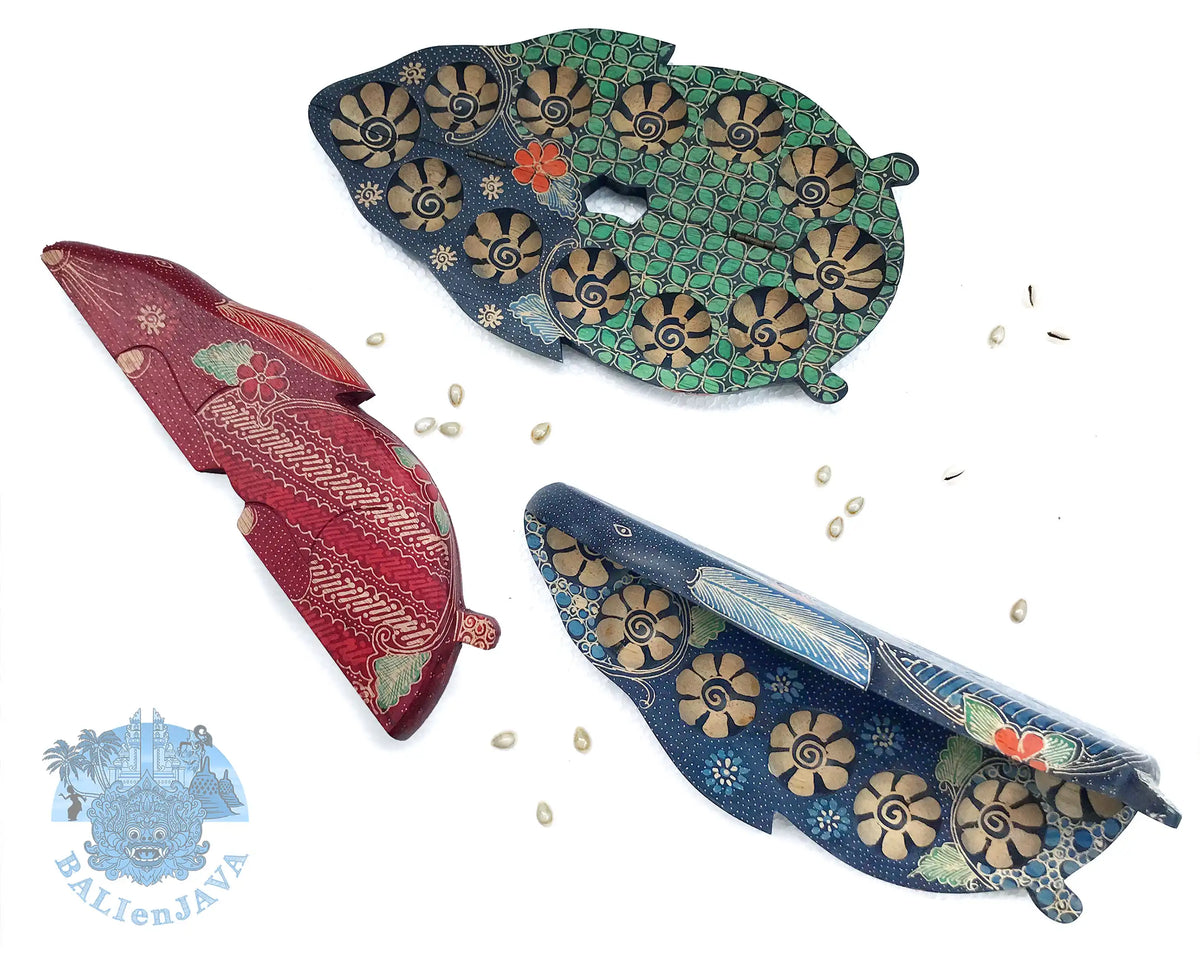 Three traditional mancala board games in hand-painted floral and geometric patterns, displayed on a white background with scattered cowrie shells.