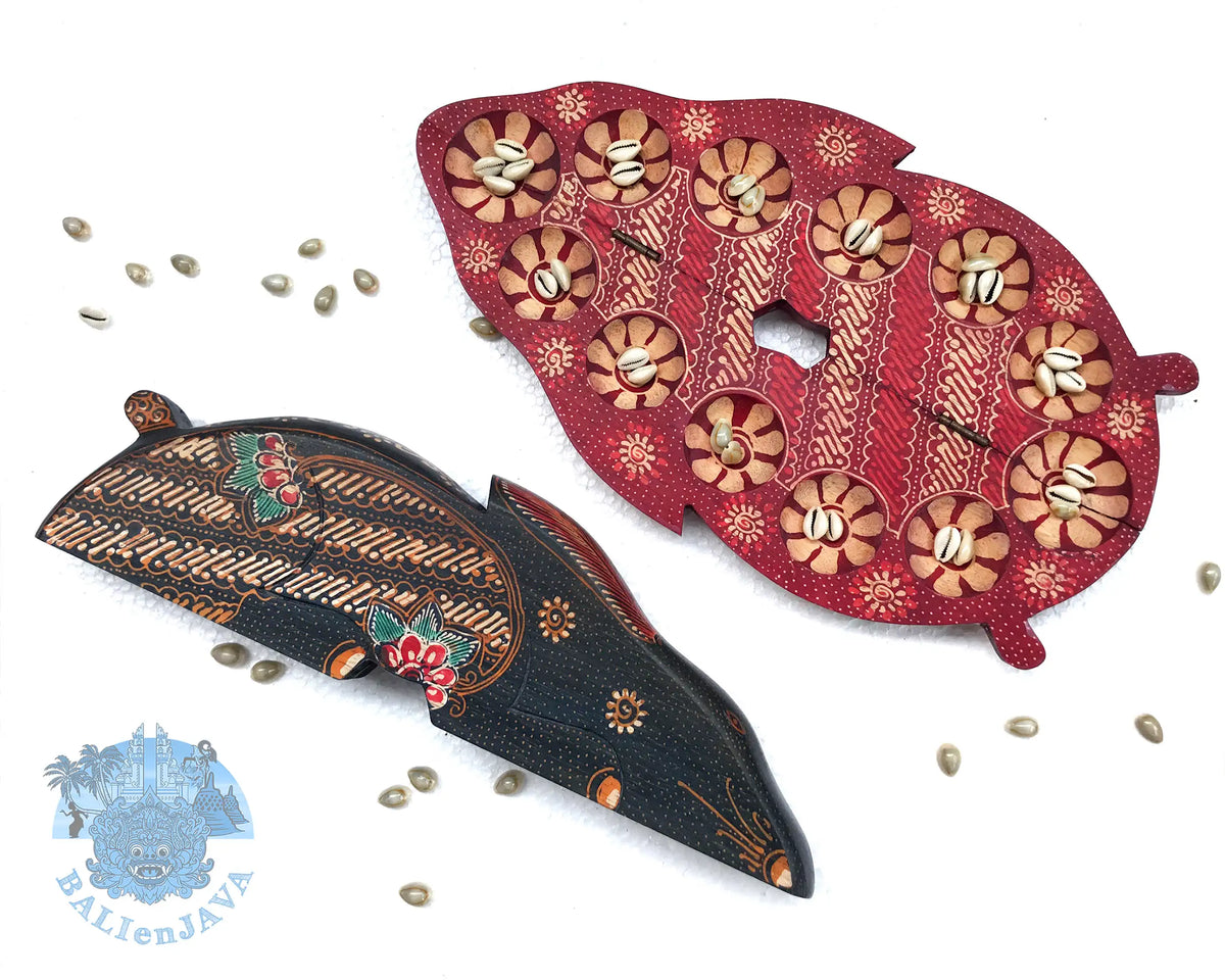 Two hand-painted rabbit-shaped board games. A red board is shown opened with circular pits, and the dark brown board is shown closed, with cowrie shells scattered on a white background.