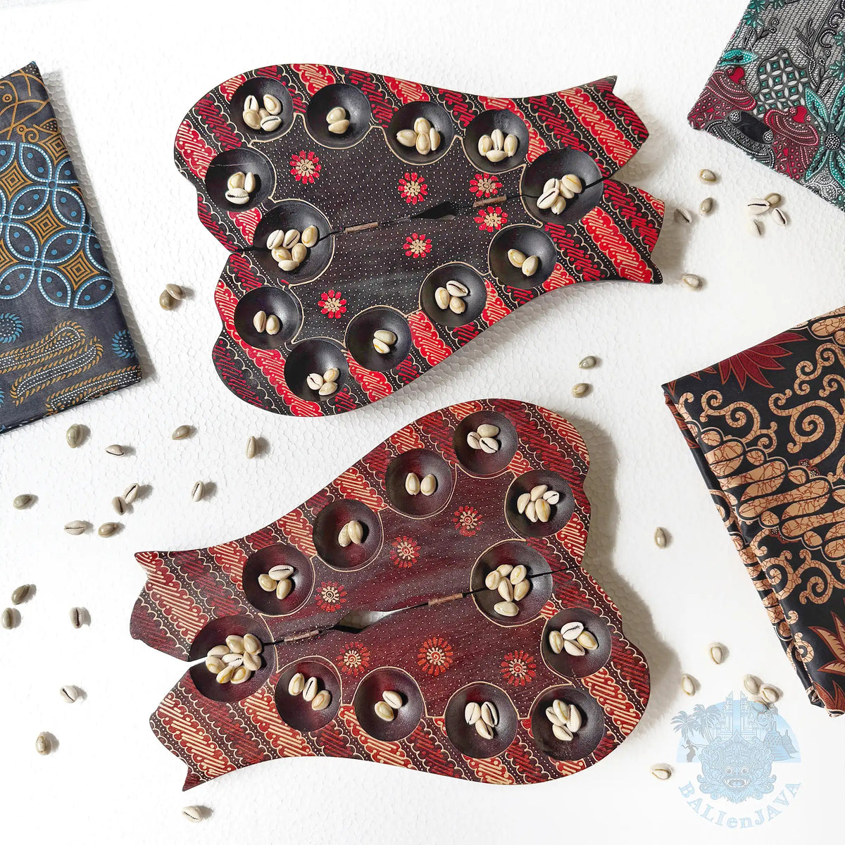 Two cat-shaped mancala board games with small circular pits, each pit contains cowrie shells, with extra shells scattered on the white background