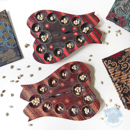 Two cat-shaped mancala board games with small circular pits, each pit contains cowrie shells, with extra shells scattered on the white background