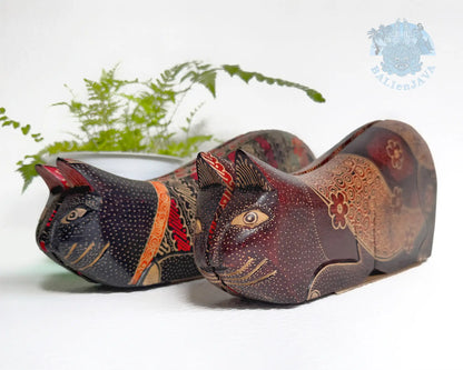 A pair of handcrafted wooden cat-shaped board games with detailed hand-painted patterns, displayed on a white surface with a green fern in the background.
