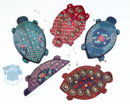 Five colorful wooden mancala board game with turtle shape, hand-painted pattern, and circular pits, displayed on a white background with small scattered cowrie shells.