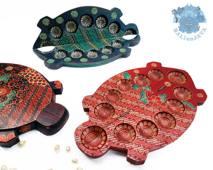 Three turtle-shaped wooden mancala board games with hand-painted details, displayed on a white background with small scattered cowrie shells.