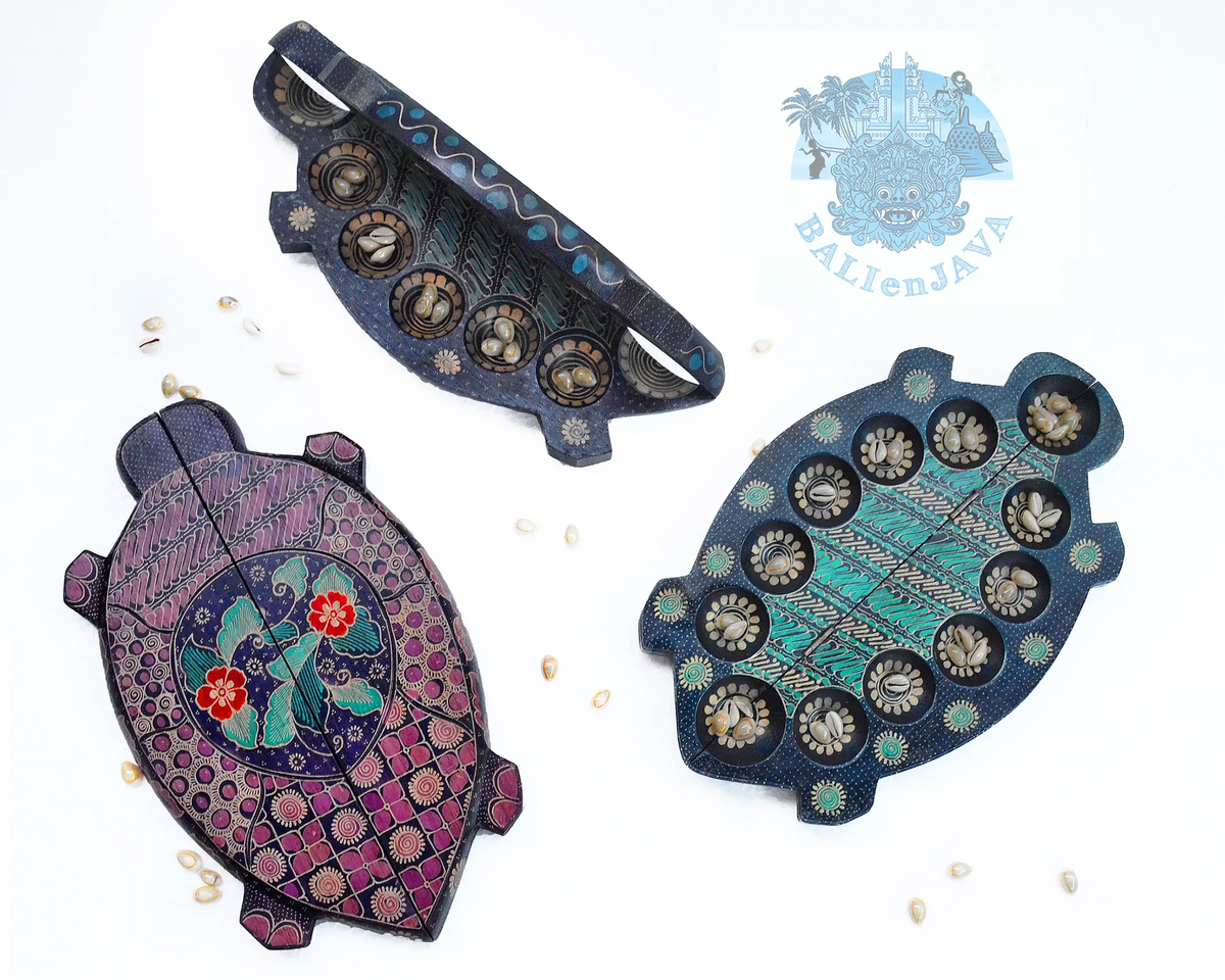 Three turtle-shaped wooden mancala board game with hand-painted details, displayed on a white background with small scattered cowrie shells.