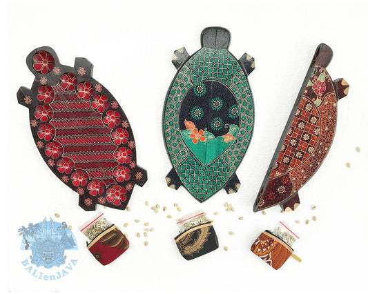 Three wooden mancala board game with patterns and hand-painted details, displayed on a white background with small scattered cowrie shells.