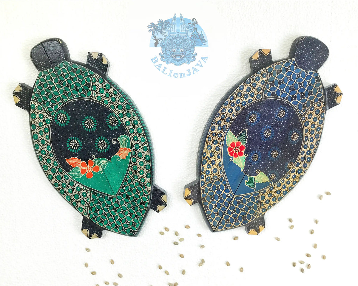 Two hand-painted turtle-shaped wooden mancala game in green and blue color on a white background, with cowrie shells scattered nearby.