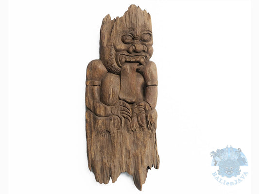 A carved wooden wall art of a mythological figure with a wide grin, large eyes, and a protruding tongue, shown against a plain white background.