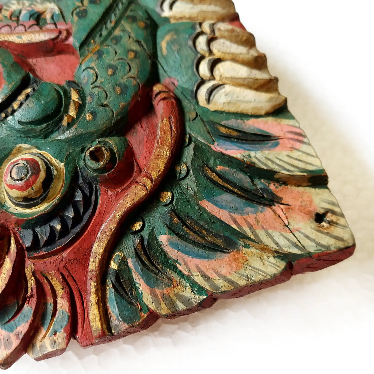 A close-up of a hand-carved wooden bell depicting a stylized dragon head, showcasing intricate hand-painted details in green, red, gold, and beige on a white background.