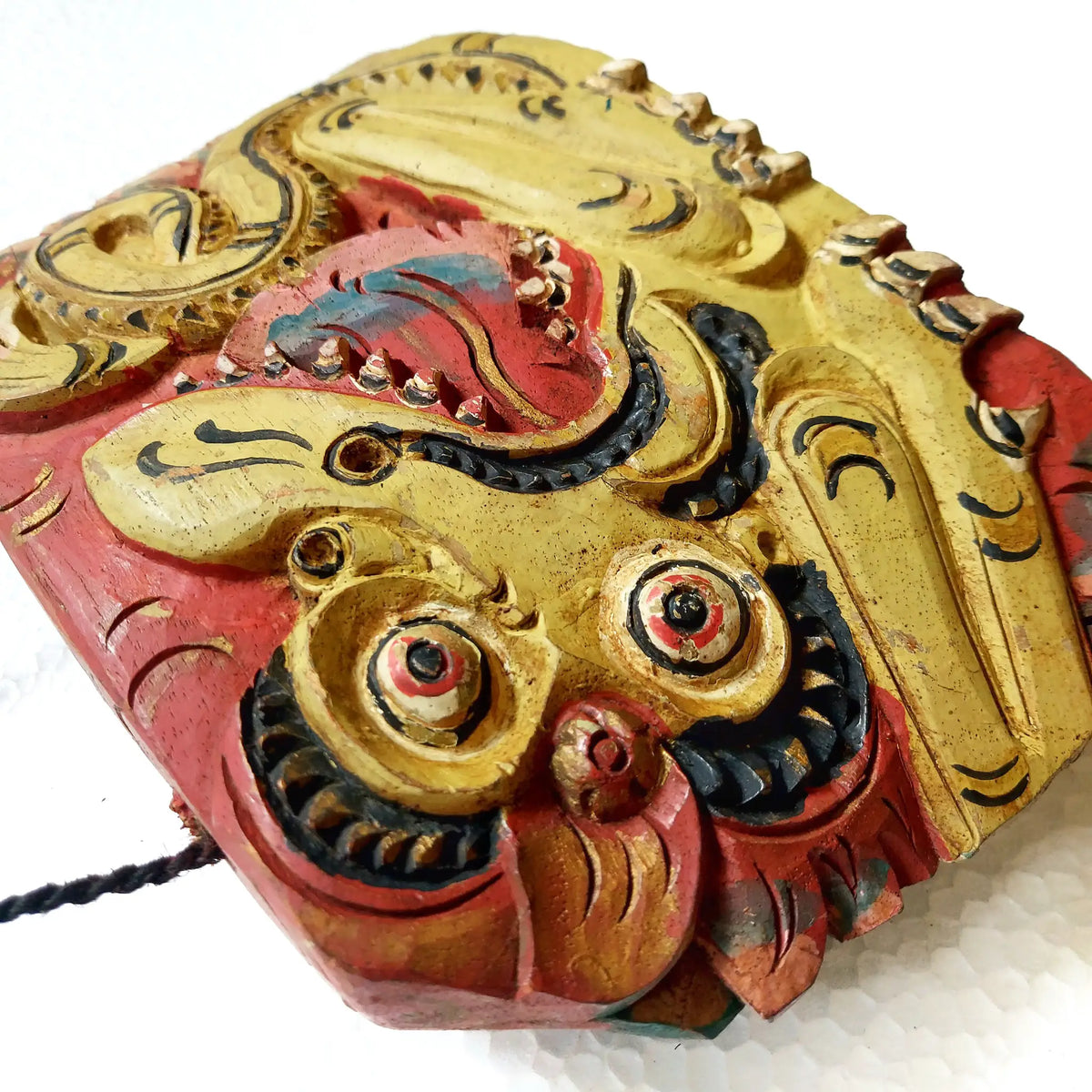 A close-up of a hand-carved wooden bell depicting a stylized dragon head, showcasing intricate hand-painted details in yellow, red, and black paint on a white background.
