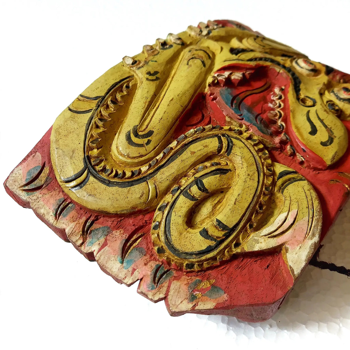A close-up of a hand-carved wooden bell depicting a stylized dragon body, showcasing intricate hand-painted details in yellow, red and black on a white background.
