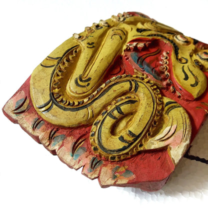 A close-up of a hand-carved wooden bell depicting a stylized dragon body, showcasing intricate hand-painted details in yellow, red and black on a white background.