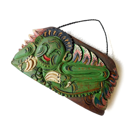 A hand-carved wooden bell with a curved bottom, featuring a mythological creature in green, reddish-brown and pink tones, set against a plain white background.