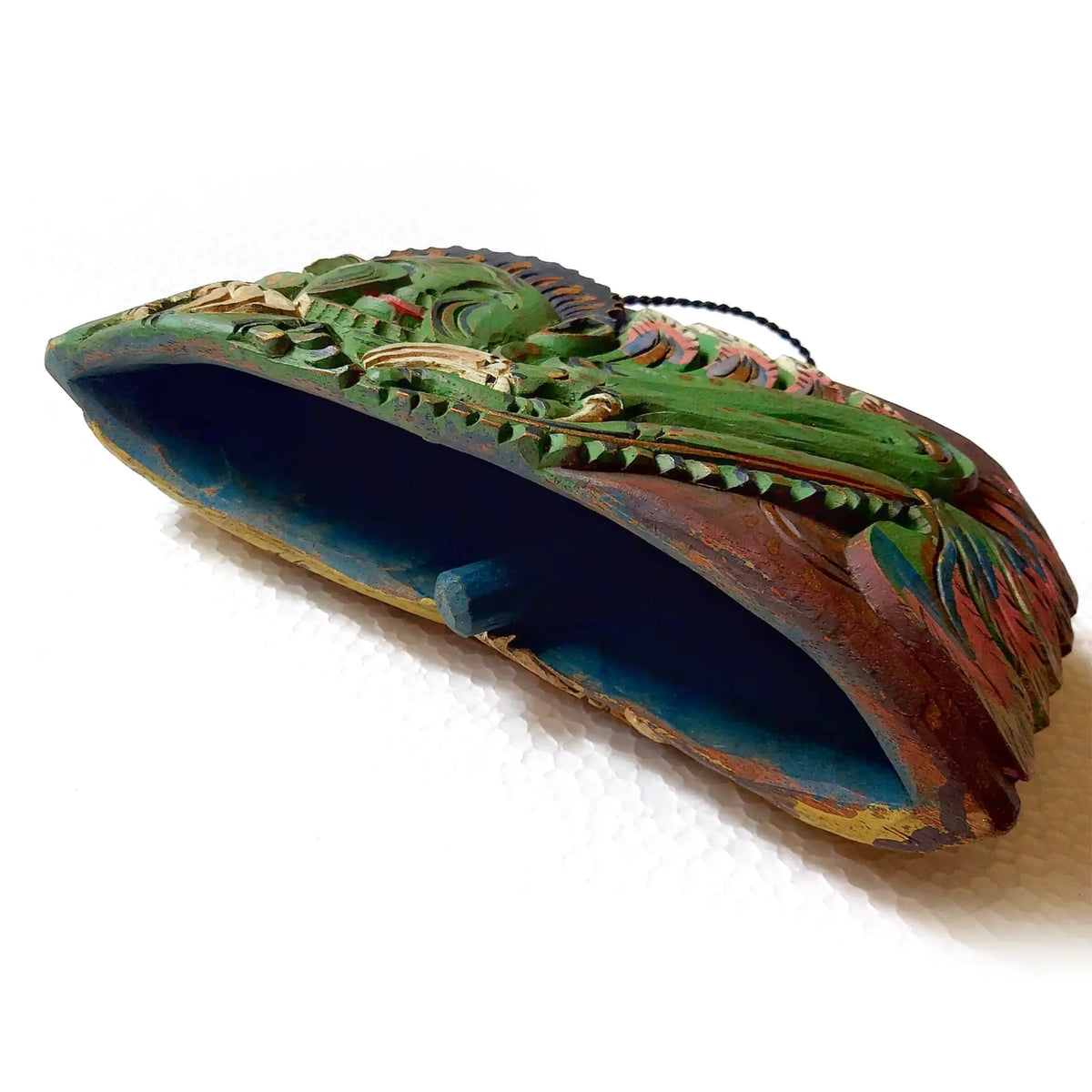 A hand-carved wooden bell object with a curved bottom, in green, blue, red, and gold tones, set against a plain white background.
