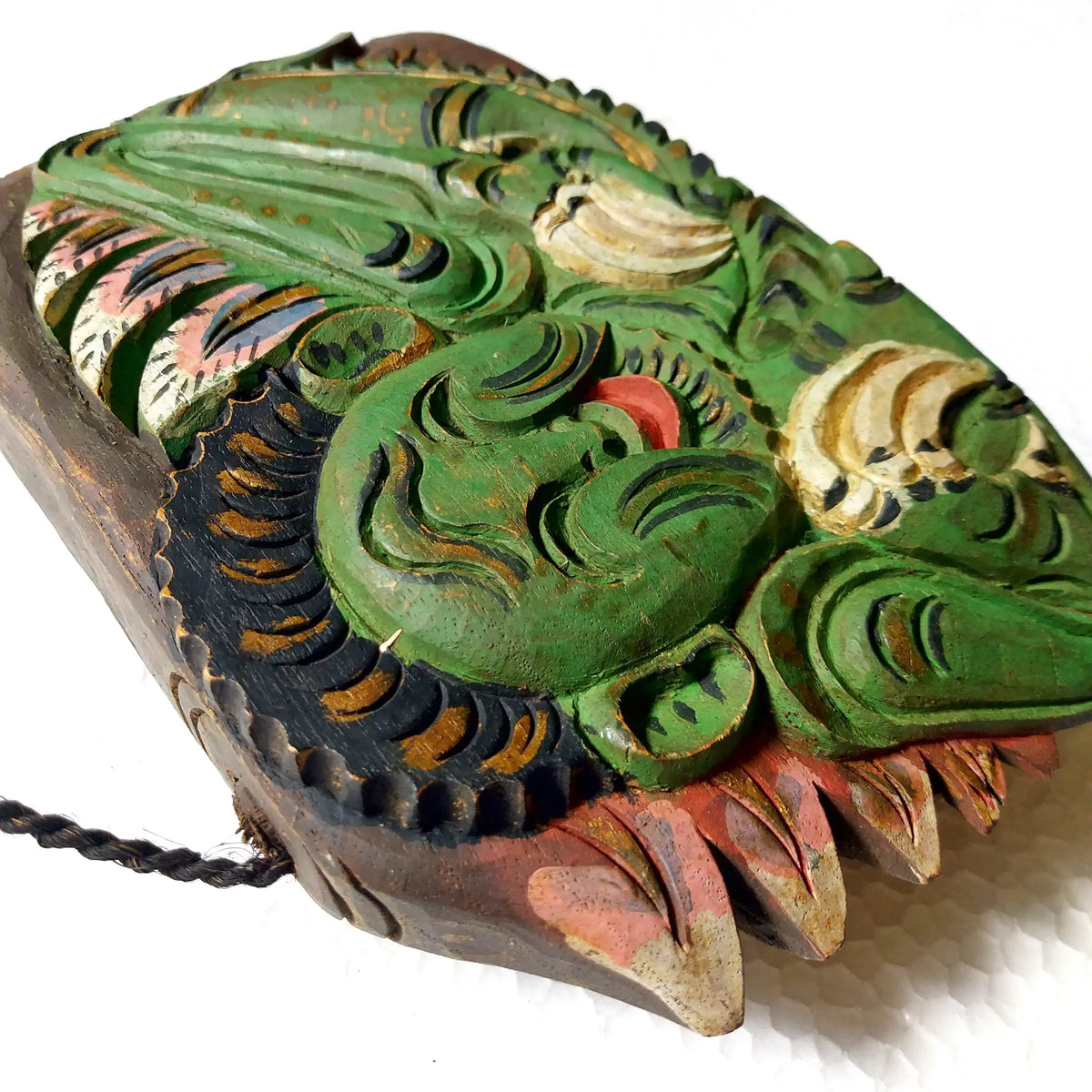 A carved wooden bell featuring a mythological creature with prominent green, black, beige, and reddish-brown painted details, photographed on a white background.