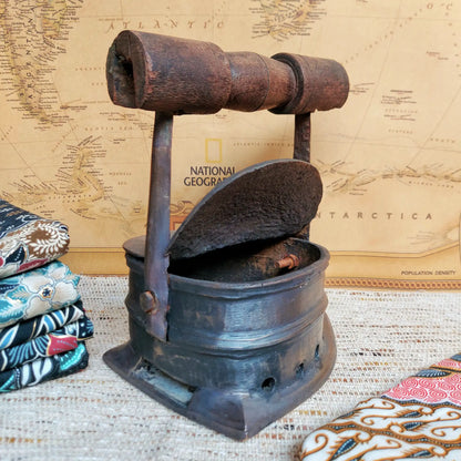 A vintage charcoal clothes iron with a dark brown wooden handle, displayed on a textured beige woven mat with a National Geographic map in the background.