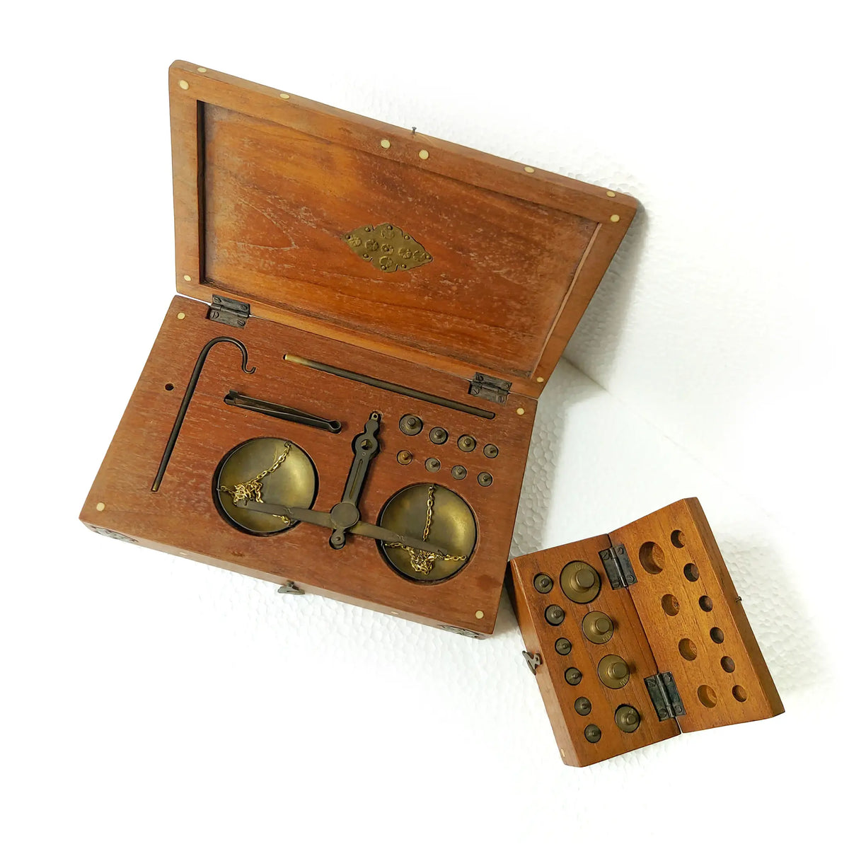 Two wooden boxes containing brass balance scales and weights, shown open with the lid propped up, and a smaller box with peg holes on a white background.