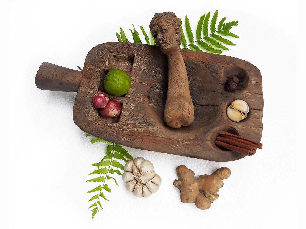 A carved wooden mortar and pestle with a sculpted human head, photographed on a plain white background.