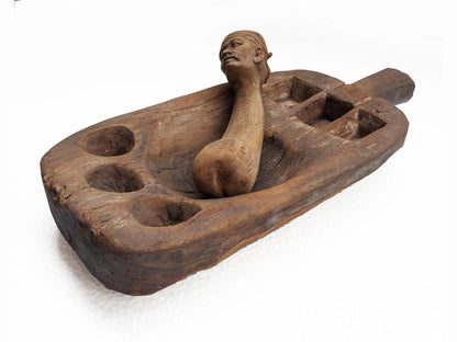 A carved wooden mortar and pestle with a sculpted human figure head, photographed on a plain white background.
