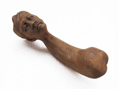 A wooden pestle carved with a realistic male head on the top, photographed on a white background.