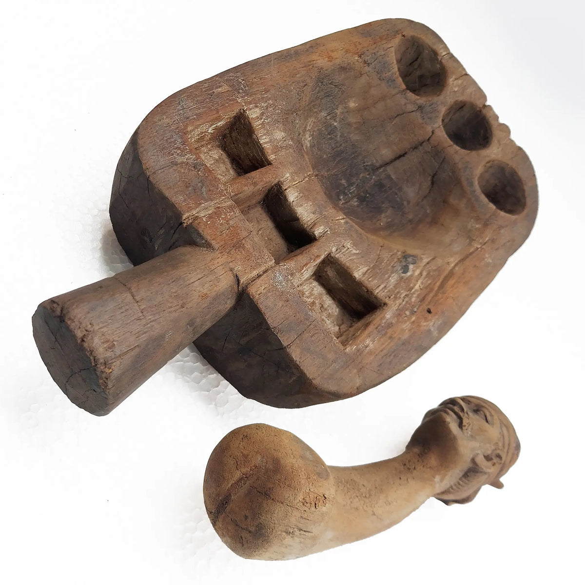 A carved wooden mortar and pestle with a sculpted human figure head, photographed on a plain white background.