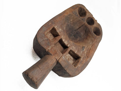 A rustic, hand-carved wooden pestle with square and circular compartments, shown on a plain white background.