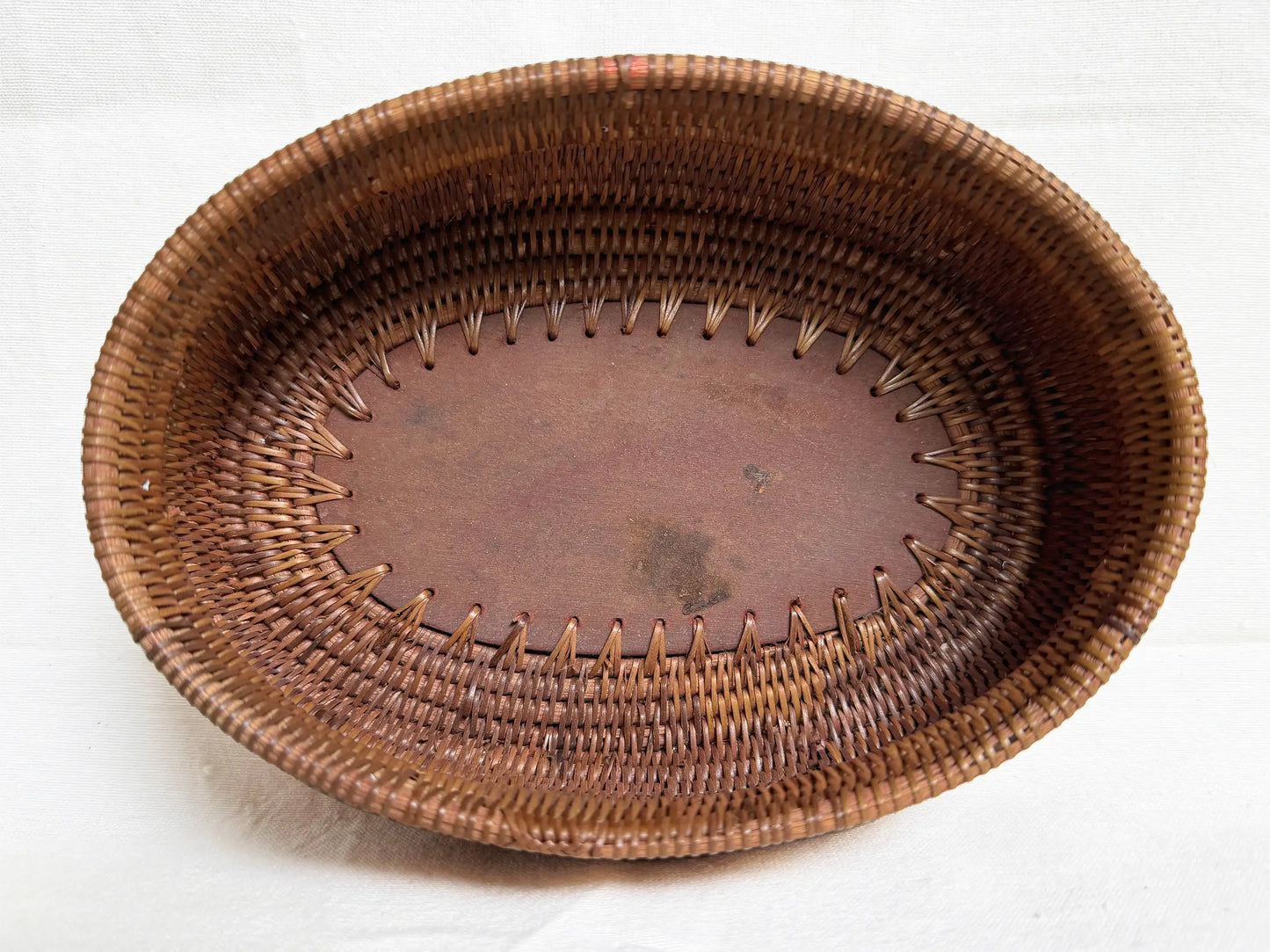 A rustic oval woven basket made of brown natural fibers, featuring a stitched decorative border and a solid wood interior, set against a plain white background.