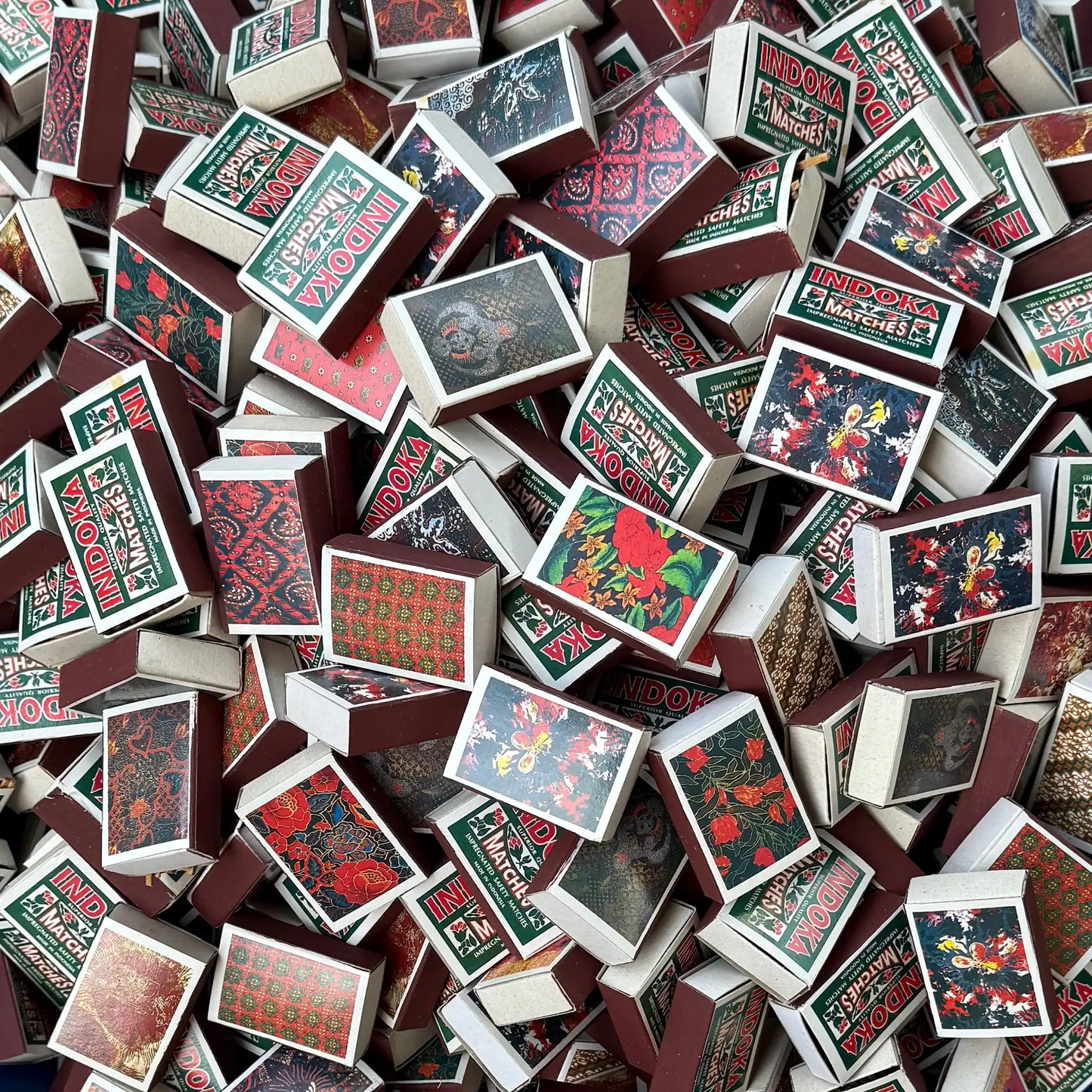 A dense pile of vintage matchboxes with floral and batik patterns.