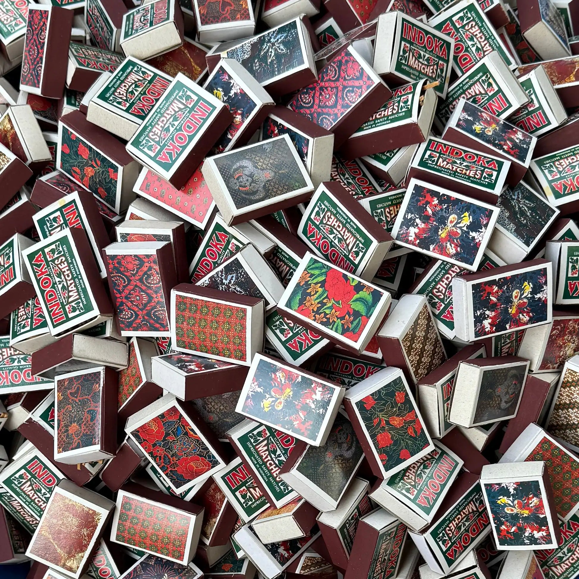 A dense pile of vintage matchboxes with floral and batik patterns.