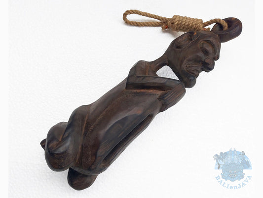 A dark brown carved wooden slit drum of a figure with a rope loop at the top, shown on a white background.