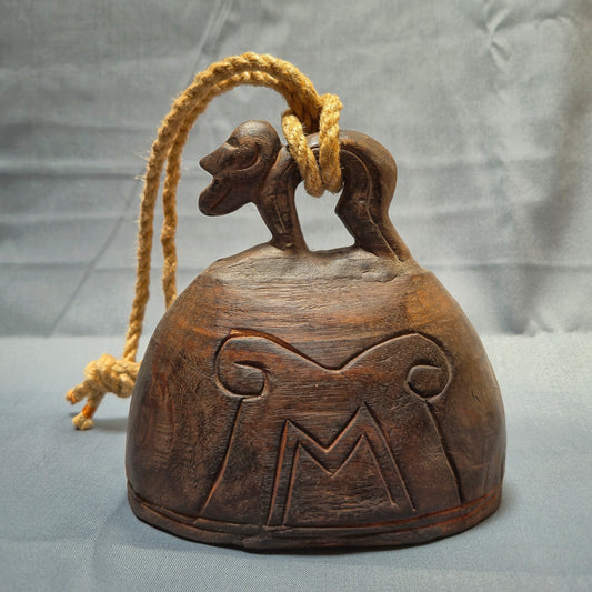 Wooden bell with rope and decorative carvings on a gray background